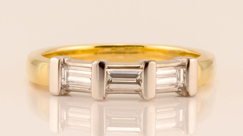 A gold wedding band set with three baguette cut diamonds.