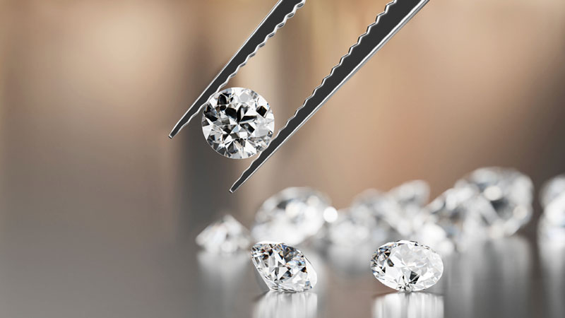 A diamond held in tweezers above other diamonds.