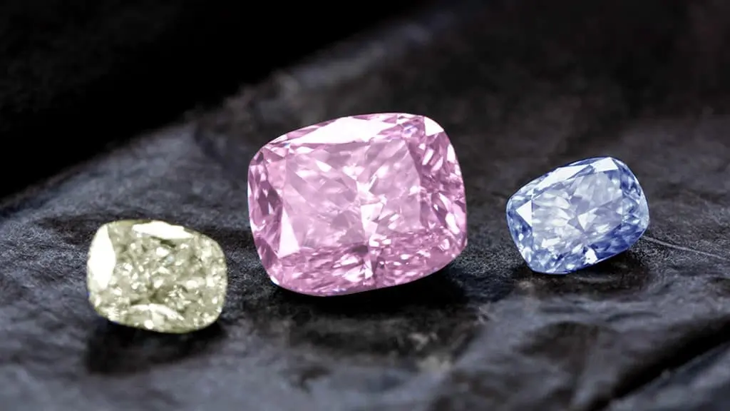 Three fancy colored diamonds arranged on a dark surface.