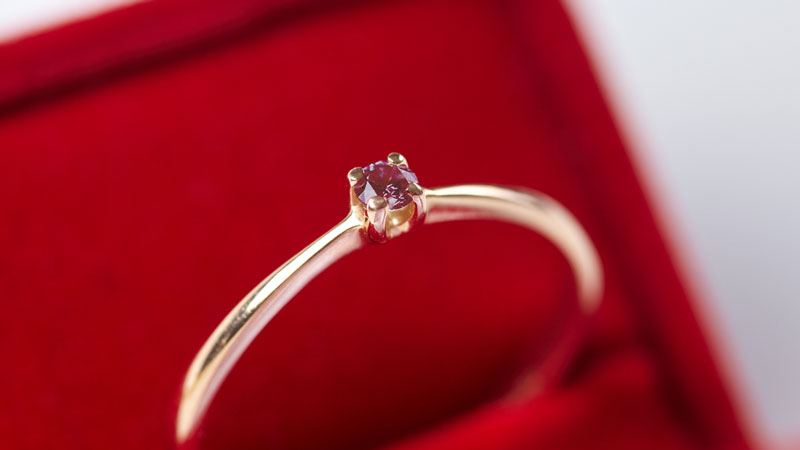 An engagement ring set with a small red diamond.
