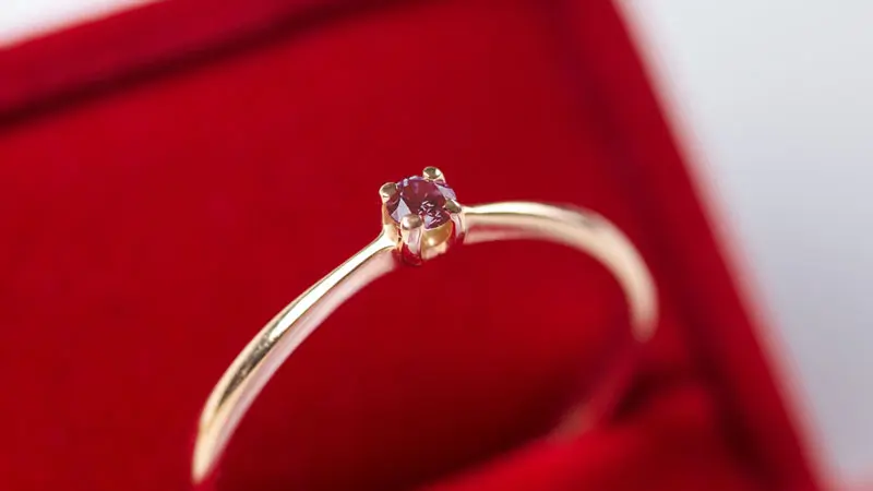 An engagement ring set with a small red diamond.
