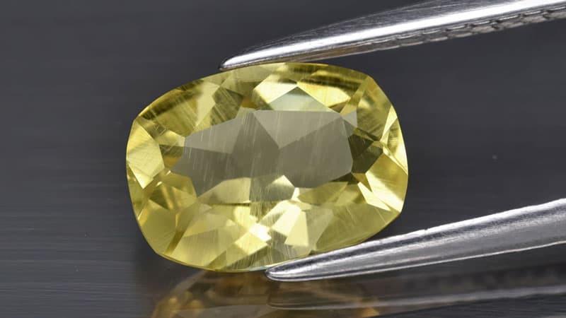 A yellow heliodor gem displayed in tweezers.