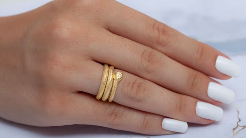 A hand wearing a 14k gold grade snake ring.